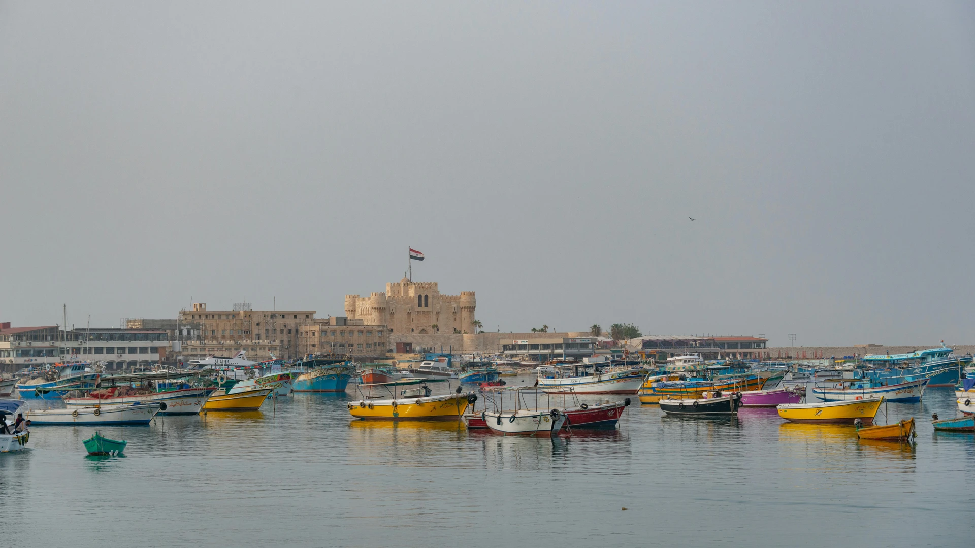 Alexandria, Egypt - Colorful boats float in alexandria's harbor with the historic citadel of qaitbay in the background.