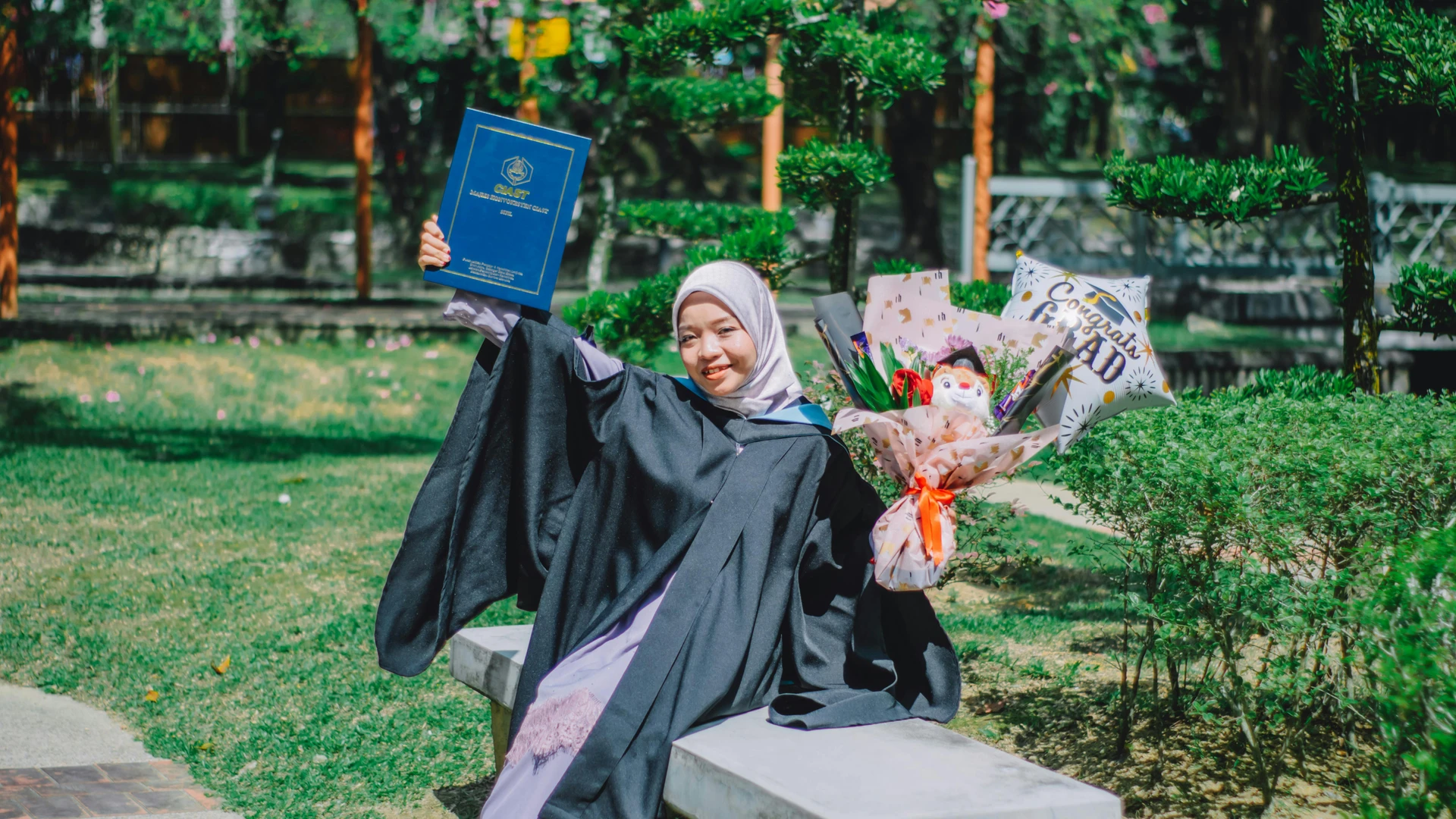 Marsa Alam, Egypt - Happy woman in graduation gown sitting on a bench, celebrating in shah alam, malaysia.