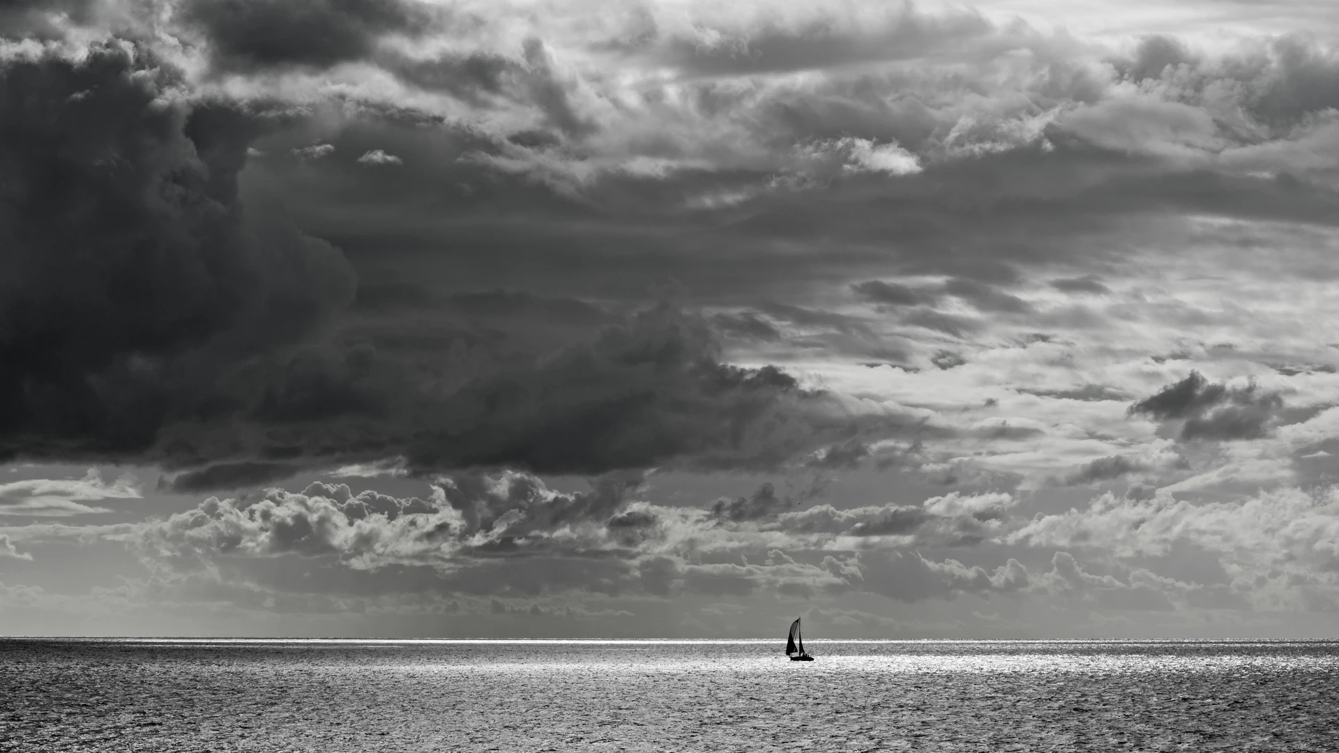 Soma Bay, Egypt - Lone sailboat navigates a vast ocean under dramatic skies in stunning black and white.