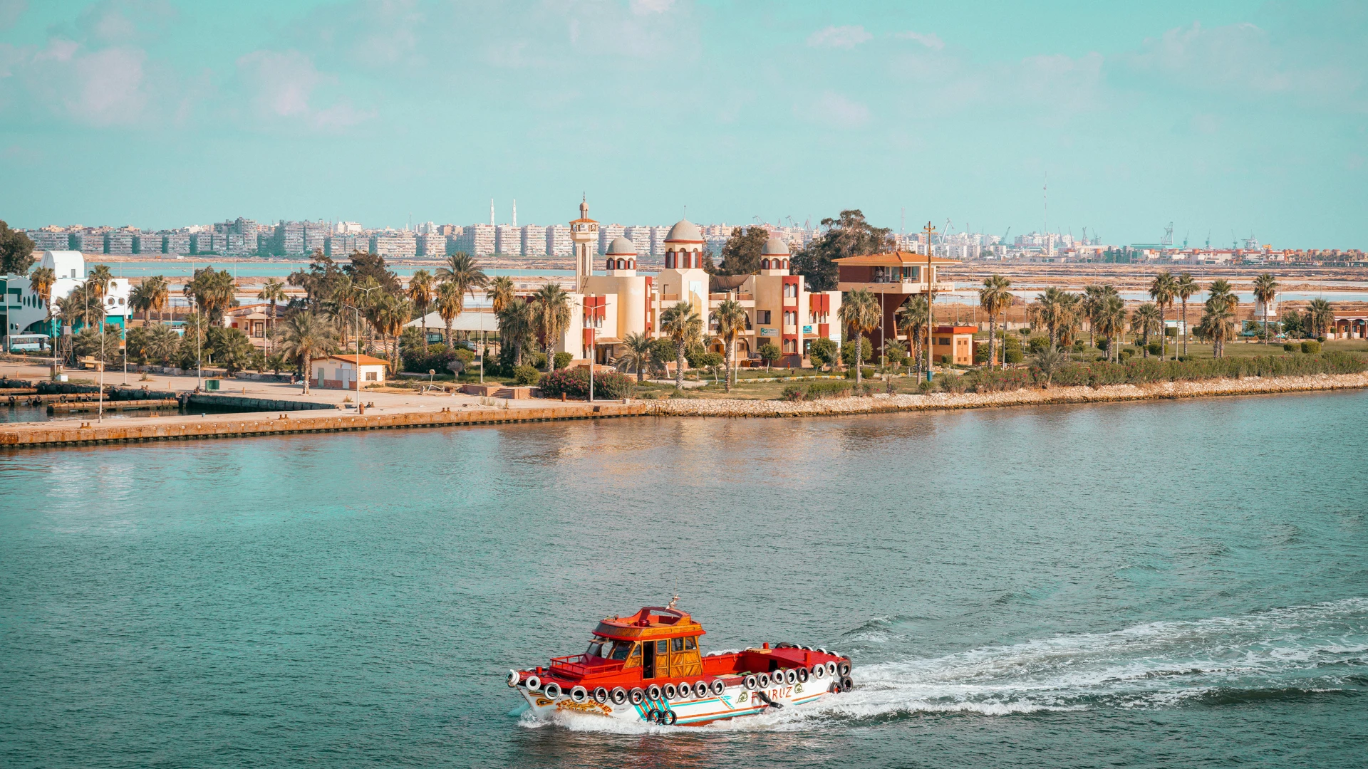 Soma Bay, Egypt - Scenic view of a red boat cruising near a city with palm trees and vibrant architecture.