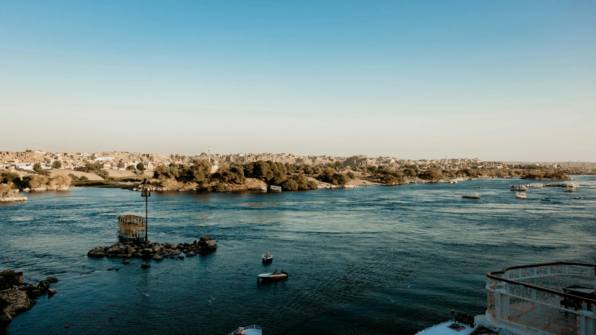 Aswan, Egypt - Picturesque view of aswan's nile river with boats and lush shoreline under a clear blue sky.
