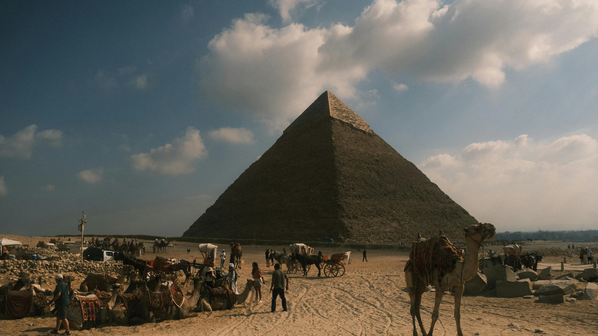 Giza, Egypt - People and camels near the iconic great pyramid of giza under a blue sky.