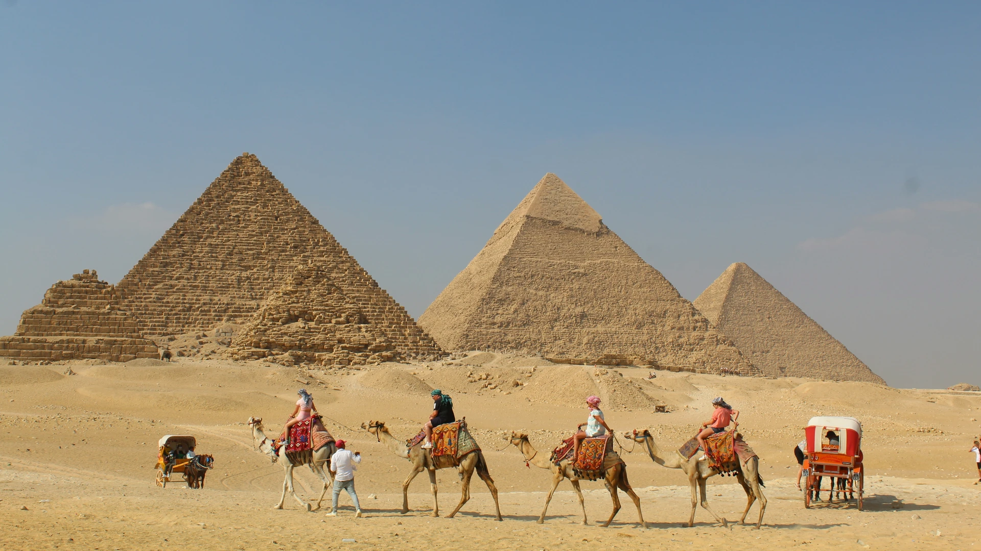 Safaga, Egypt - People riding camels past pyramids under a clear sky.