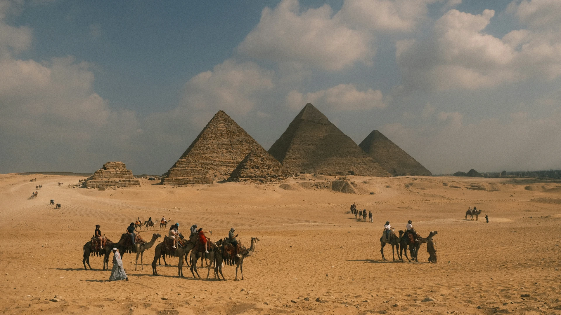 Safaga, Egypt - Camels and riders trek across desert towards pyramids.