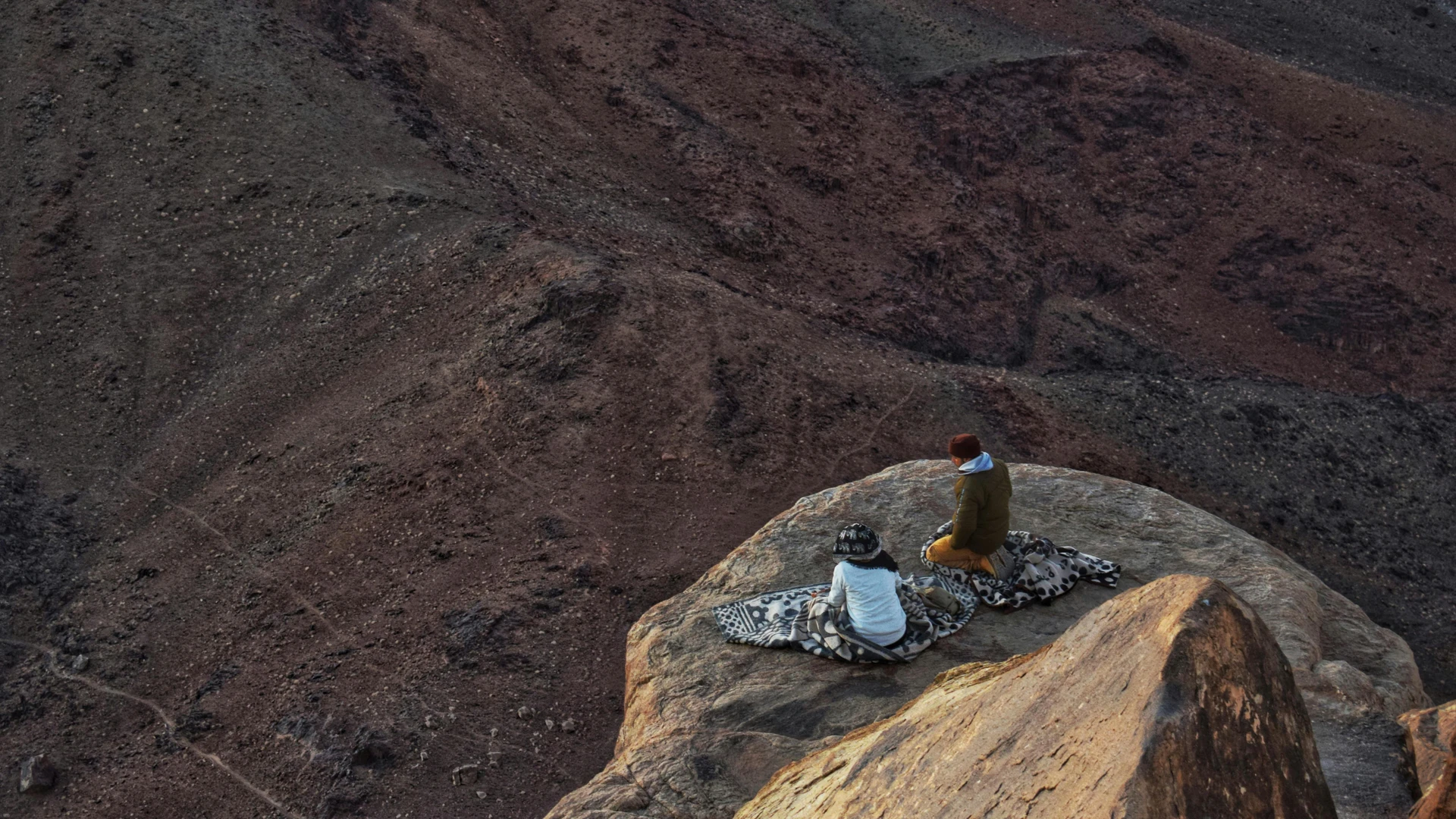 South Sinai, Egypt - Two people wrapped in blankets sit on a rocky mountaintop in saint catherine, sinai.